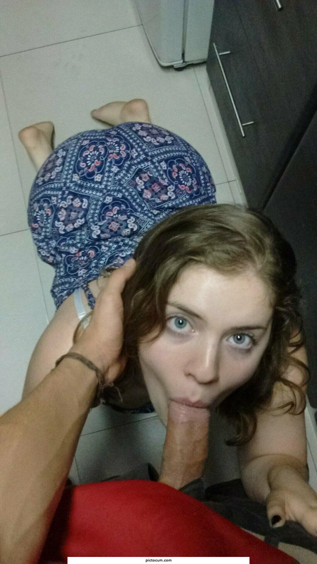 On her knees maintaining eye contact with a cock in her mouth like a good girl